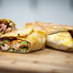 Pyszny kebab w tortilli z kurczakiem, warzywami i cebulą, ułożony na desce.