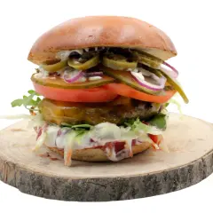 Burger z jalapeño, pomidorem, cebulą i sałatą na drewnianym krążku.