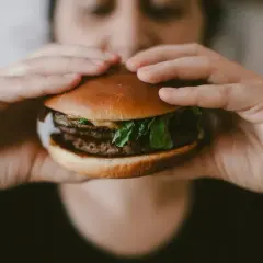 Ręce trzymają soczystego burgera, przypominającego mcroyal sklad. Mięso, sałata i bułka wyglądają apetycznie.