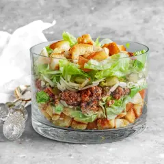 Warstwowa sałatka a'la Big Mac w szklanej misie, z mielonym mięsem, sałatą, serem, ogórkiem i grzankami.