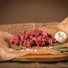 Surowe mielone mięso na papierze, obok czosnek, sól i liście laurowe.