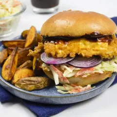 Drwal z kurczakiem w panierce, z serem, czerwoną cebulą i surówką coleslaw, podany z pieczonymi ziemniakami.