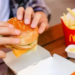 Ręce trzymają burgera z McDonald's, obok frytki i sos śmietanowy McDonald. Idealny zestaw na szybki posiłek.