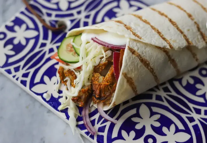 Pyszny kebab w picie z soczystym mięsem, chrupiącą surówką, pomidorem, ogórkiem i czerwoną cebulą, zawinięty w ciepły placek.