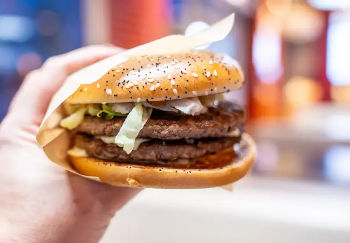 Dłoń trzyma soczystego big arch burgera z dwoma kotletami i chrupiącą sałatą.