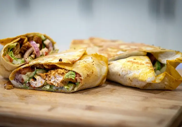 Pyszny kebab w tortilli z kurczakiem, warzywami i cebulą, ułożony na desce.