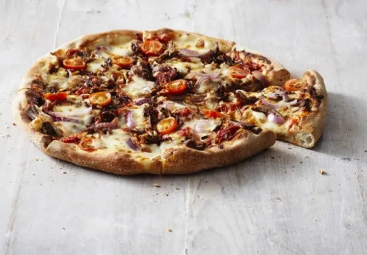 Pizza Hut ciasto San Francisco z pomidorkami, cebulą i serem. Pyszna, gorąca pizza na drewnianym blacie.