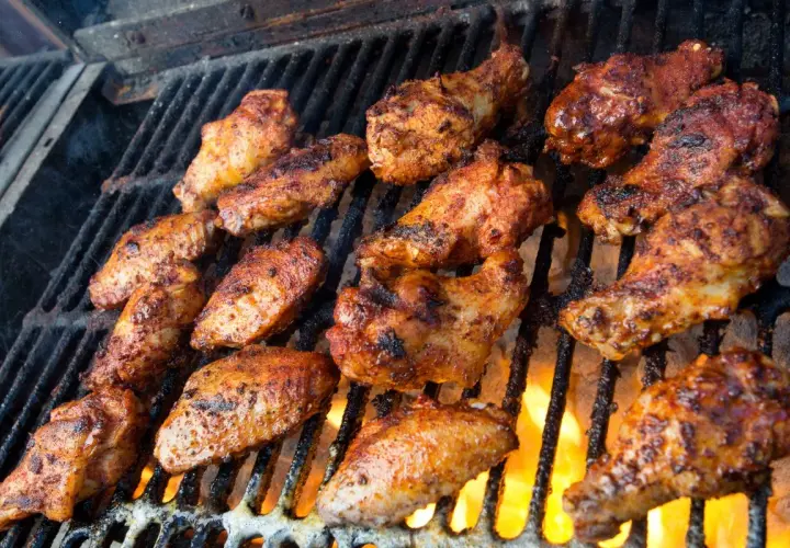 Skrzydełka kurczaka w marynacie do skrzydełek pieką się na grillu, z ogniem buchającym spod rusztu.