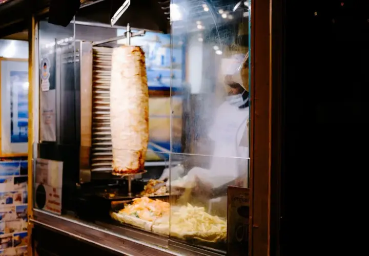 Obracający się pionowo kebab z frytkami i sałatką w witrynie.