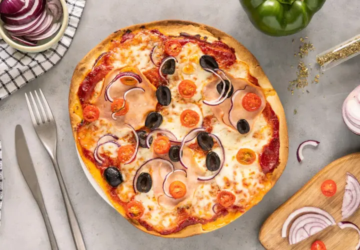 Gotowa pizza z szynką, oliwkami, pomidorkami i czerwoną cebulą na gotowym spodzie.
