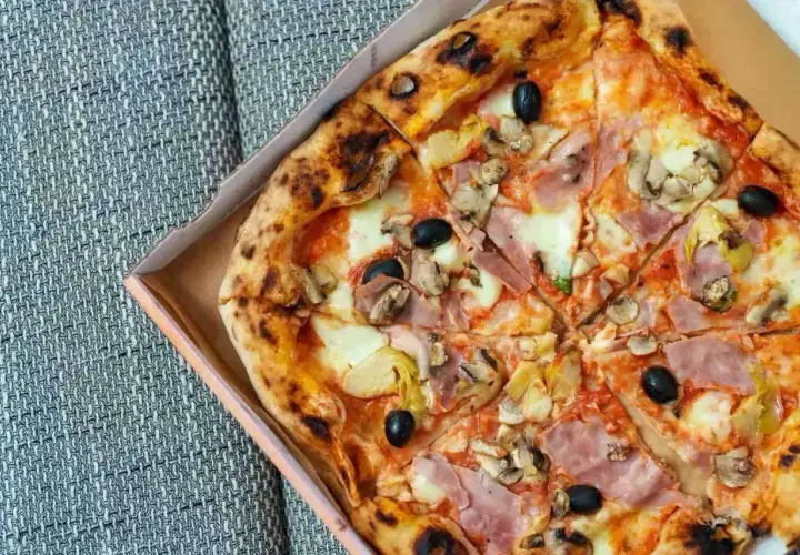 Pyszna pizza capricciosa z szynką, pieczarkami, karczochami i oliwkami w pudełku.