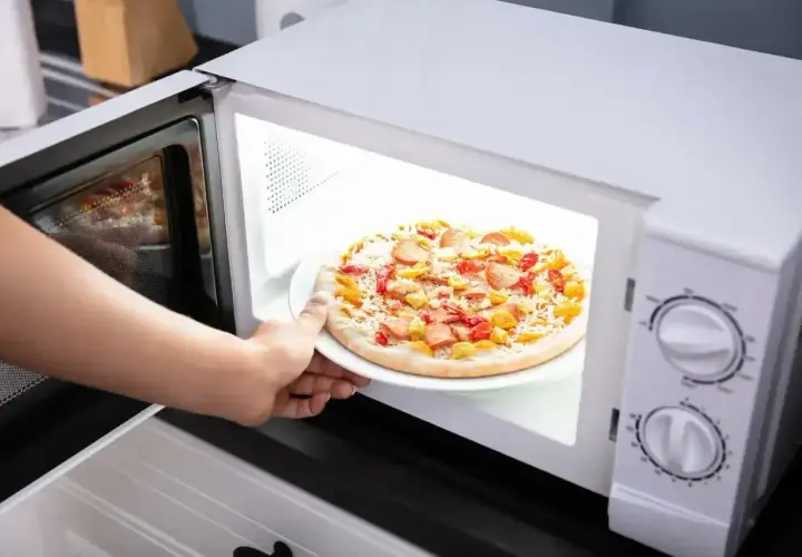 Ręka wkłada talerz z pizzą Giuseppe do mikrofali.