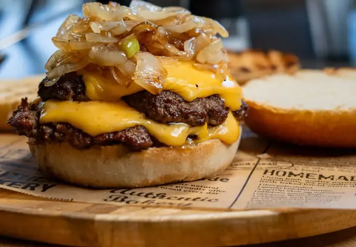 Smash burger z podwójną wołowiną, serem cheddar i karmelizowaną cebulką na bułce.