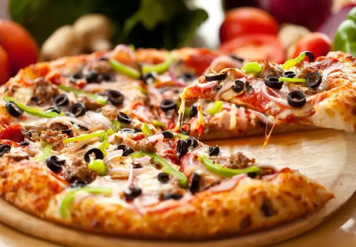 Idealny pizza day! Gorąca, ciągnąca się pizza z mnóstwem dodatków, w tym oliwkami i papryką, czeka na zjedzenie.