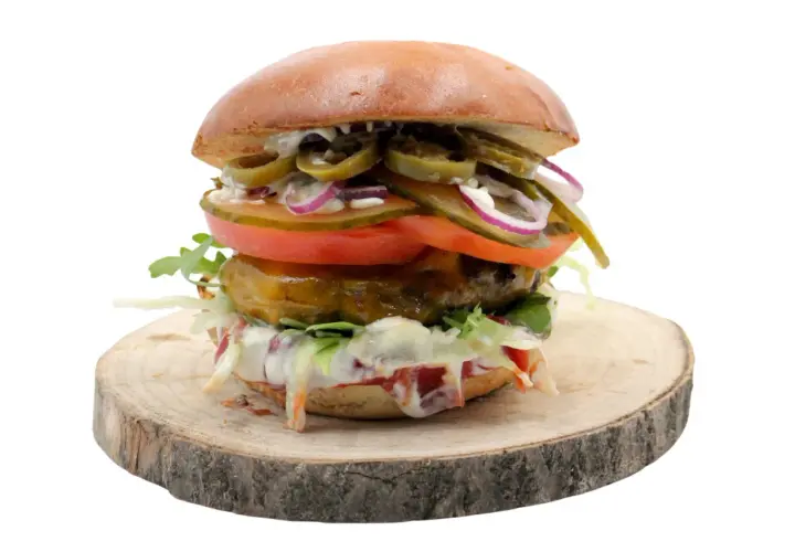 Burger z jalapeño, pomidorem, cebulą i sałatą na drewnianym krążku.