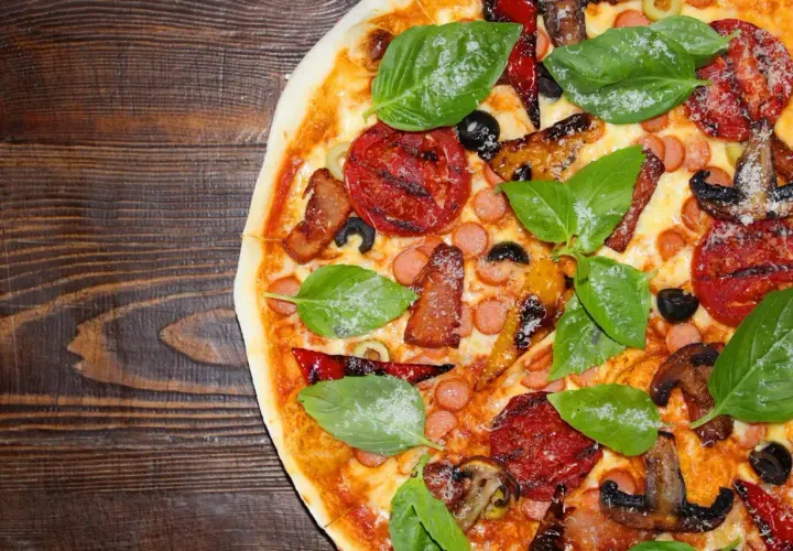Pyszne rodzaje pizzy: z pomidorami, kiełbaską, boczkiem, oliwkami i bazylią na drewnianym blacie.