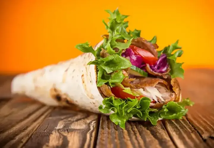 Pyszny kebab zawinięty w placek, z soczystym mięsem, chrupiącą sałatą, pomidorem i czerwoną kapustą. Tak wygląda idealny kebab!