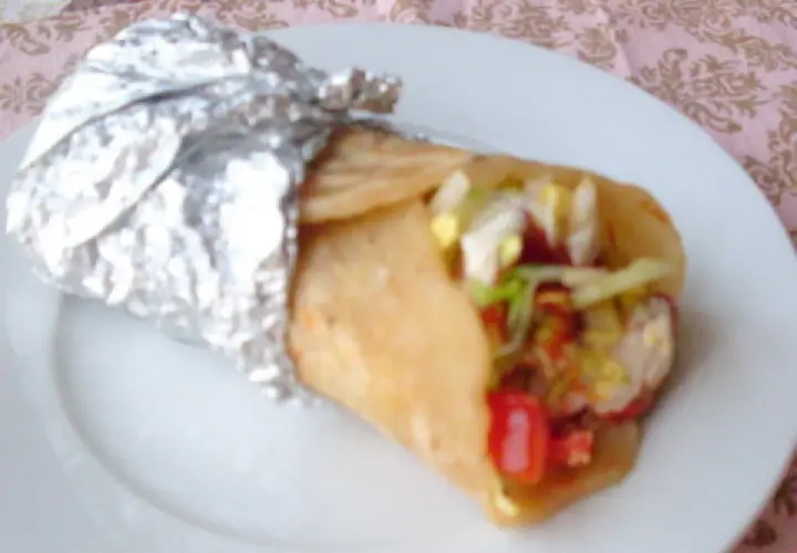 Pyszny placek z kebabem, zawinięty w folię aluminiową, z widocznym nadzieniem z warzyw i mięsa.