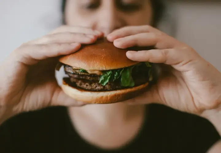 Ręce trzymają soczystego burgera, przypominającego mcroyal sklad. Mięso, sałata i bułka wyglądają apetycznie.