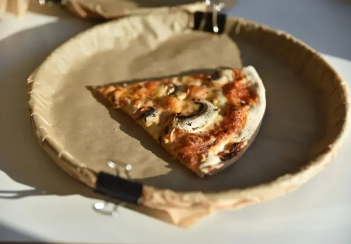 Kawałek pizzy 50 cm, z pieczarkami i serem, na papierowym talerzu. Zastanawiasz się nad jej kcal?