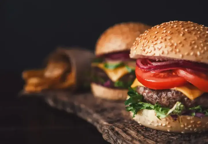 Dwa soczyste burgery iberyjskie z serem, pomidorem i czerwoną cebulą, obok porcji frytek.