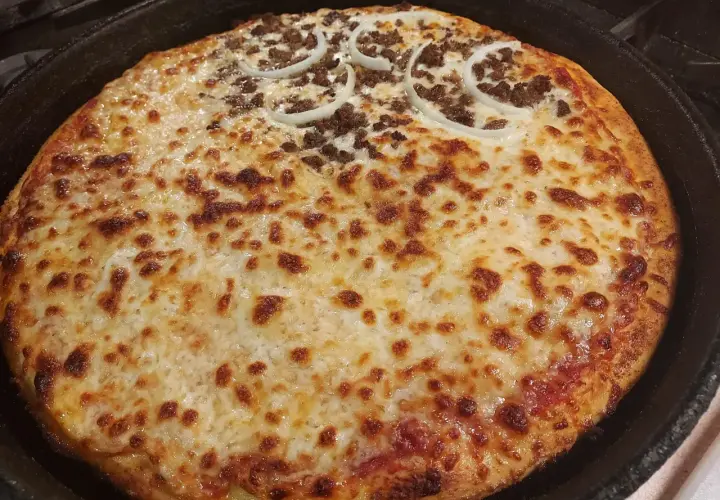 Pyszna pizza supreme z Pizza Hut, z mięsem mielonym i krążkami cebuli, zapieczona na złoto w żeliwnej patelni.