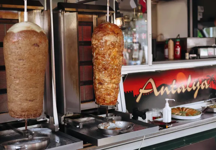 Dwa pionowe rożna z mięsem na kebab, obok znak "Antalya". Zastanawiasz się, ile kosztuje kebab?