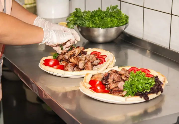 Ręce w rękawiczkach układają mięso na plackach z pomidorami i natką. Pyszny gemuse kebab gotowy do podania.