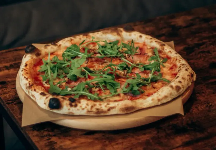 Pyszna pizza z rukolą i szynką, dzieło prawdziwego pizzaiolo, na drewnianym stole.