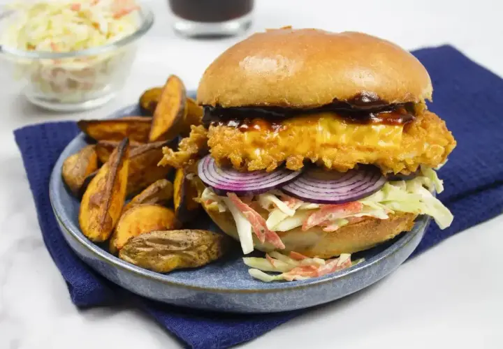 Drwal z kurczakiem w panierce, z serem, czerwoną cebulą i surówką coleslaw, podany z pieczonymi ziemniakami.