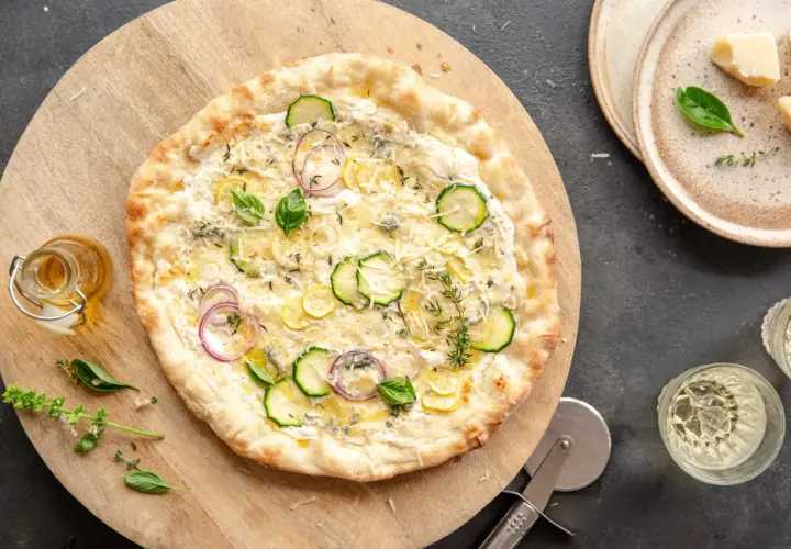 Pyszna pizza bianca z cukinią, cebulą i cytryną, ozdobiona bazylią i tymiankiem.