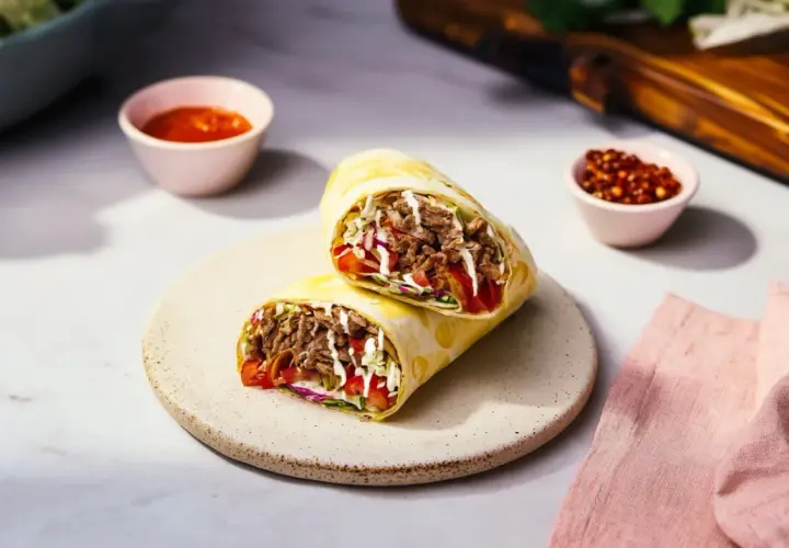 Pyszny durum z mięsem, warzywami i sosem, podany na talerzu. Obok miseczki z sosem i papryczkami chili.