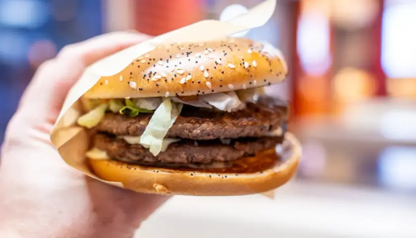 Dłoń trzyma soczystego big arch burgera z dwoma kotletami i chrupiącą sałatą.