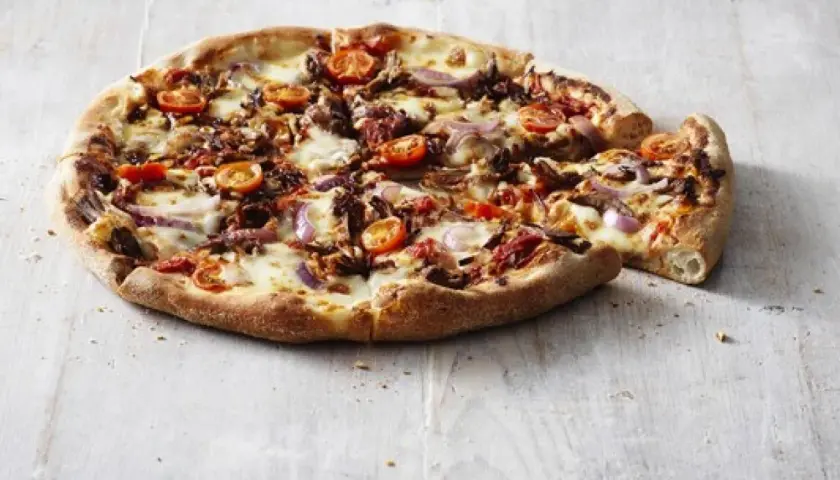 Pizza Hut ciasto San Francisco z pomidorkami, cebulą i serem. Pyszna, gorąca pizza na drewnianym blacie.
