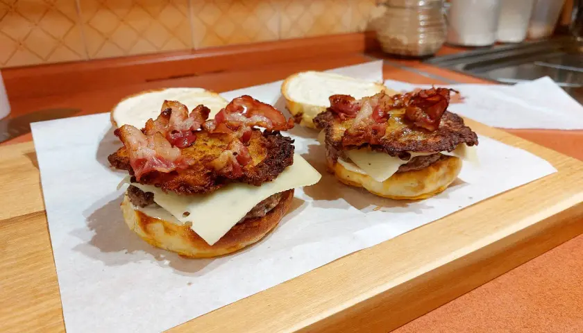 Dwa domowe burgery, przypominające kanapkę zbójnicką z McDonald's, z serem, plackiem ziemniaczanym i chrupiącym boczkiem.