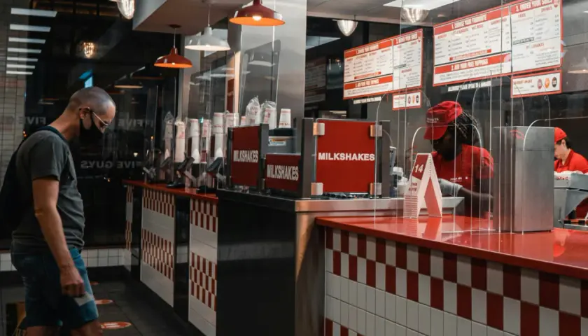 Klient w masce w Five Guys Polska czeka na zamówienie. W tle widać menu i pracownika za ladą.