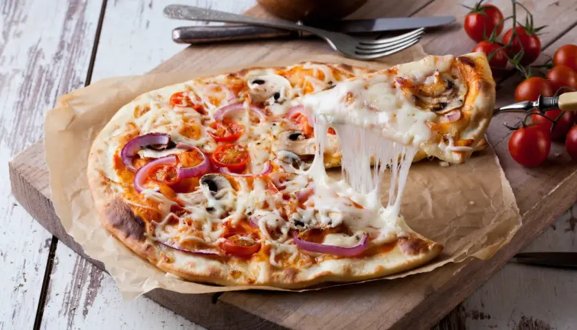 Rozciągający się ser z pizzy z pomidorami, cebulą i pieczarkami na desce.