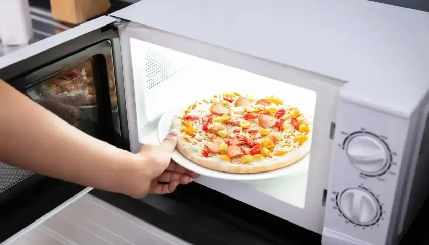 Ręka wkłada talerz z pizzą Giuseppe do mikrofali.