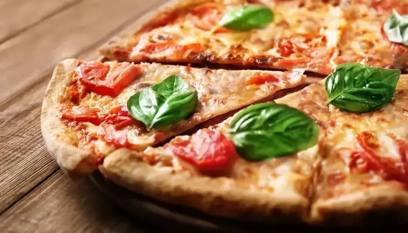 Klasyczna pizza Margherita, jak z Pizza Hut, z pomidorami i bazylią na drewnianym blacie.