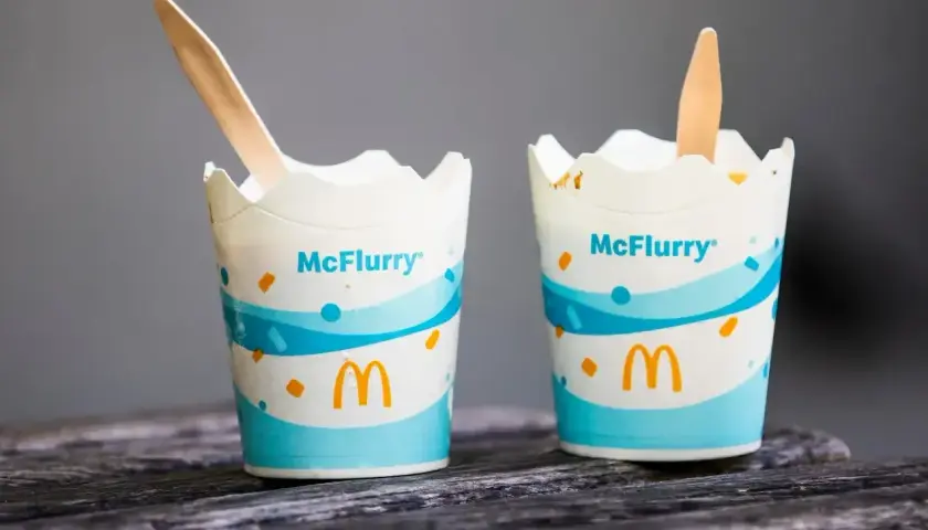Dwa kubki McFlurry McDonald's z drewnianymi łyżeczkami na drewnianym blacie.