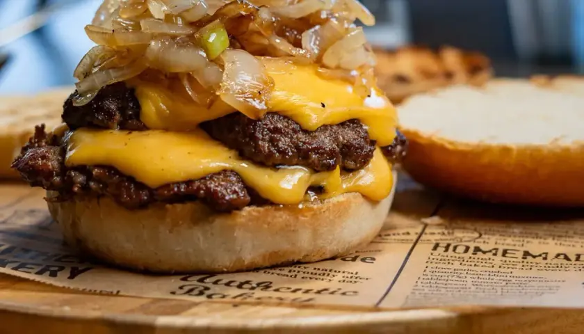 Smash burger z podwójną wołowiną, serem cheddar i karmelizowaną cebulką na bułce.