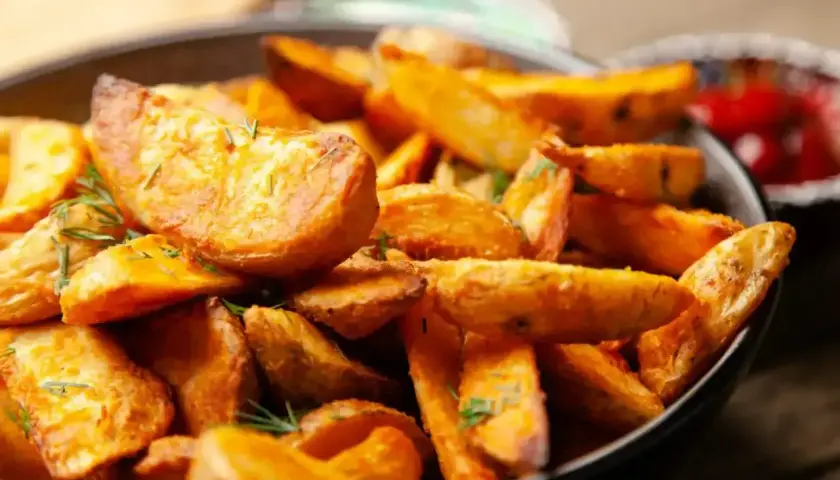 Chrupiące frytki stekowe z ziołami w misce, obok ketchup.