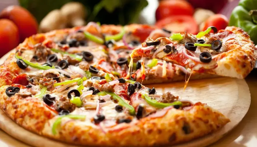 Idealny pizza day! Gorąca, ciągnąca się pizza z mnóstwem dodatków, w tym oliwkami i papryką, czeka na zjedzenie.