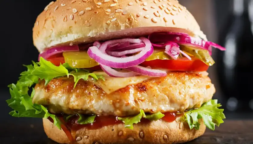 Pyszny burger z kurczakiem, sałatą, pomidorem, ogórkiem, czerwoną cebulą i roztopionym serem. Jaki ser jest w drwalu? To tajemnica, ale wygląda na pyszny!