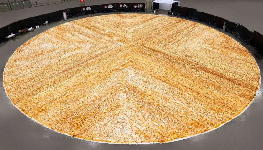 Gigantyczna pizza, największa na świecie, rozłożona na ogromnej przestrzeni. Jej złocisty kolor i równomierne posypanie przyprawami zachwycają.