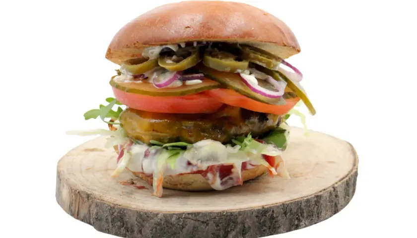 Burger z jalapeño, pomidorem, cebulą i sałatą na drewnianym krążku.