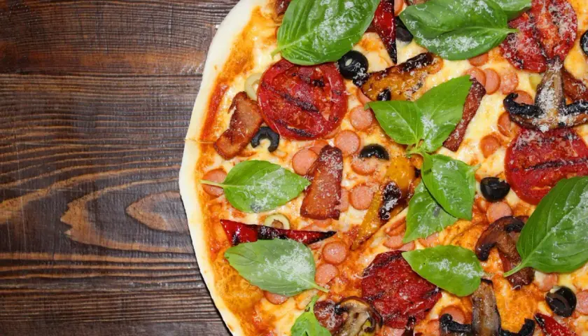 Pyszne rodzaje pizzy: z pomidorami, kiełbaską, boczkiem, oliwkami i bazylią na drewnianym blacie.