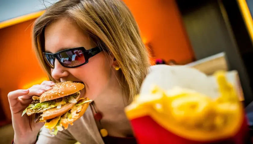 Dziewczyna w okularach je pysznego mcmuffin wieprzowy z jajkiem. Obok frytki.