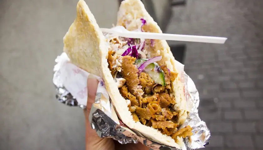 Pyszny kebab w bułce z mięsem, warzywami i sosem. To danie, które swoją popularność zawdzięcza podróżom i wymianie kulturowej, pokazując, skąd pochodzi kebab.