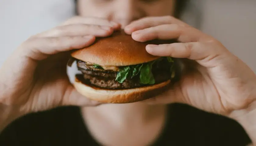 Ręce trzymają soczystego burgera, przypominającego mcroyal sklad. Mięso, sałata i bułka wyglądają apetycznie.